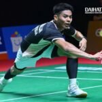 Foto ilustrasi atlet bulutangkis melakukan pukulan sambil menjangkau kok di lapangan indoor.