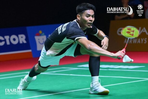 Foto ilustrasi atlet bulutangkis melakukan pukulan sambil menjangkau kok di lapangan indoor.