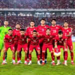 Ilustrasi 11 pemain Timnas Indonesia mengenakan seragam merah dan penjaga gawang berseragam hijau di lapangan stadion.
