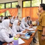 Ilustrasi guru mengajar dan berinteraksi dengan siswa di kelas dalam kegiatan pembelajaran.