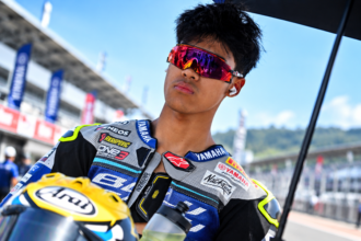 Pembalap dengan wearpack Yamaha dan kacamata merah di area sirkuit balap.