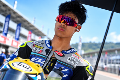 Pembalap dengan wearpack Yamaha dan kacamata merah di area sirkuit balap.