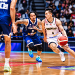 Pemain basket Indonesia berseragam putih menggiring bola saat dijaga pemain Thailand berseragam biru dalam pertandingan di lapangan indoor.