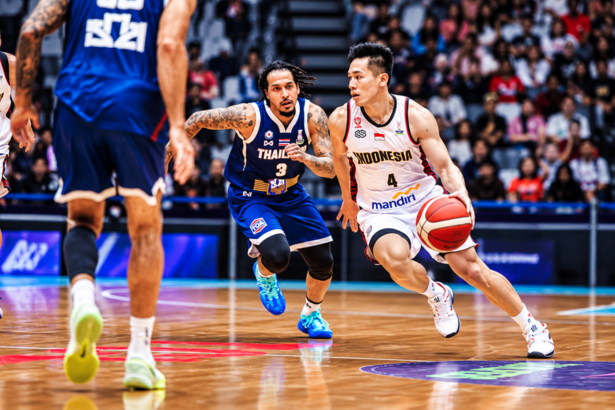 Pemain basket Indonesia berseragam putih menggiring bola saat dijaga pemain Thailand berseragam biru dalam pertandingan di lapangan indoor.