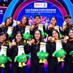 Ilustrasi tim bulu tangkis Indonesia berpose mengenakan medali dan memegang maskot di podium Badminton Asia Team Championships 2026.
