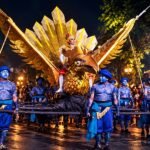 Ilustrasi parade Wayang Jogja Night Carnival dengan replika burung garuda berwarna emas dan penampil berkostum biru.