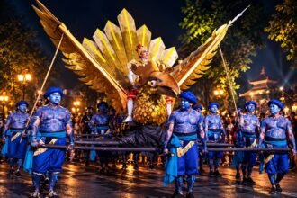 Ilustrasi parade Wayang Jogja Night Carnival dengan replika burung garuda berwarna emas dan penampil berkostum biru.