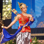 Ilustrasi penari tradisional mengenakan kostum merah berhias emas, mahkota, kain batik, dan selendang biru dalam pertunjukan seni budaya.
