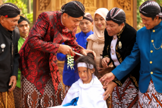 Ilustrasi prosesi pemotongan rambut anak dalam upacara tradisi ruwatan rambut gimbal dengan pakaian adat Jawa.