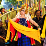 Ilustrasi penari tradisional mengenakan hiasan kepala berwarna emas dan membawa selendang kuning dalam pertunjukan budaya.