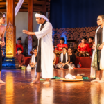 Ilustrasi pertunjukan drama tradisional Jawa dengan tiga pemeran di panggung dan pemain gamelan di latar belakang.
