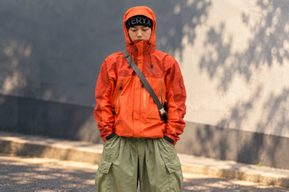 Ilustrasi pria mengenakan jaket outdoor oranye dan celana kargo hijau dengan gaya gorpcore yang menjadi tren fashion 2026.