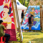 Foto ilustrasi seniman muda melukis mural berwarna-warni pada festival seni di ruang terbuka.