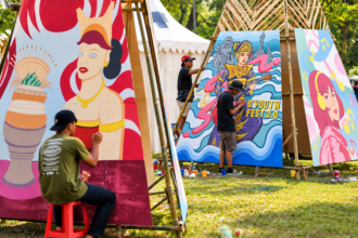 Foto ilustrasi seniman muda melukis mural berwarna-warni pada festival seni di ruang terbuka.