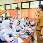 Foto ilustrasi seorang guru berseragam cokelat sedang mengajar siswa SMA di ruang kelas.