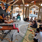 Foto ilustrasi masyarakat berkumpul dan berdiskusi di pendopo tradisional Jawa dengan ornamen budaya dan alat musik.