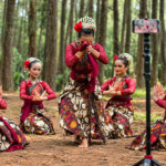 Penari tradisional mengenakan busana batik merah saat menampilkan tarian di tengah hutan pinus.